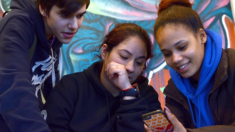 Photo of three young adult learners collaborating around a phone screen